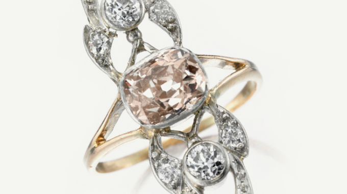 Elegant gold ring with a central pink gemstone and intricate diamond accents.