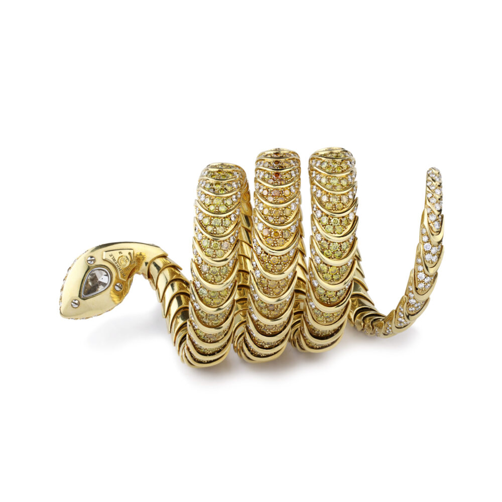 Designed as a flexible gold snake bracelet set with a pear-shaped natural brownish diamond to the head, the coiled body enhanced by yellow diamonds and white diamonds, mounted in yellow gold, circa 1990