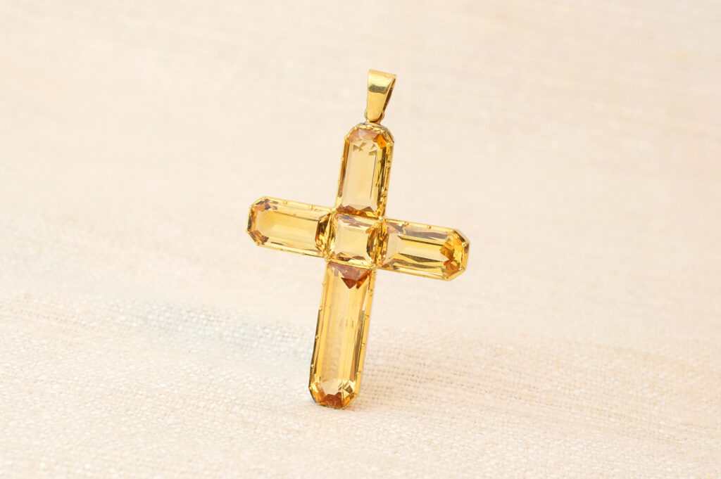 Golden crystal cross pendant with faceted edges on a beige background.